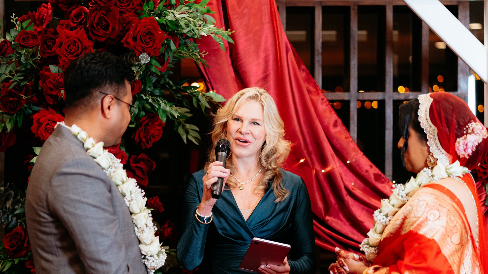 Nicole Webster smiling as she speaks to the couple at a red rose arch