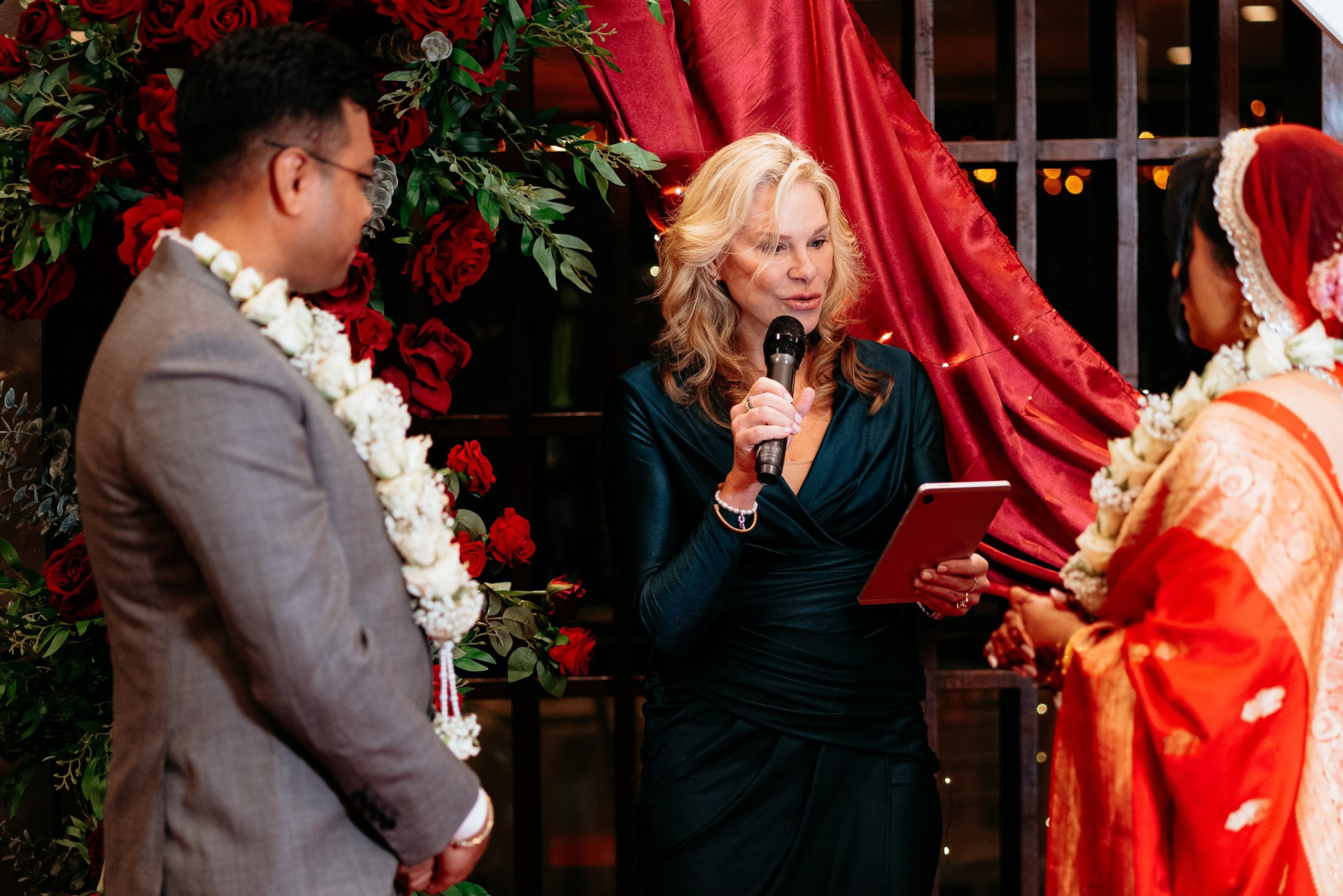 Nicole Webster leading a wedding ceremony at a red rose arch