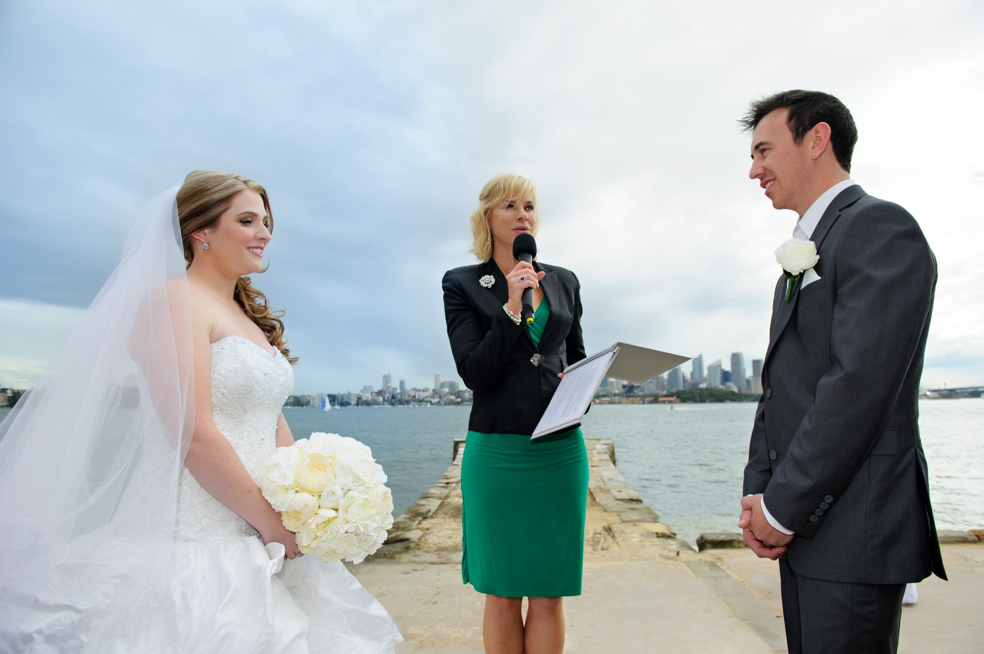 Nicole Webster officiating a harbourside pier ceremony with Sydney skyline backdrop
